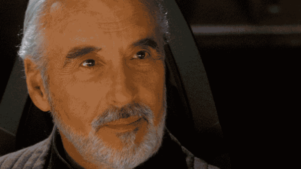 Gif d'un homme âgé ressemblant au comte Dooku de Star Wars, avec des cheveux blancs et une barbe, portant des vêtements sombres d'inspiration médiévale et une chaîne autour du cou, assis et hochant subtilement la tête