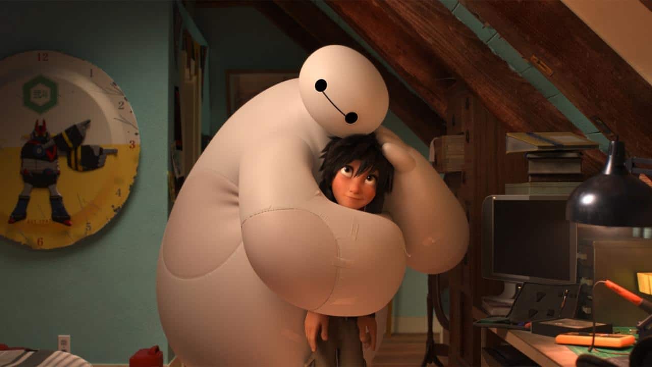 Une scène du film d'animation "Les Nouveaux Héros" montrant un grand robot super-héros gonflable blanc serrant dans ses bras un garçon brun dans une pièce encombrée éclairée par une lumière chaude.