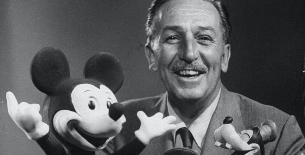 Photo en noir et blanc d'un homme souriant tenant une figurine de Mickey Mouse, exprimant sa joie et son enthousiasme dans un parc à thème Walt Disney.
