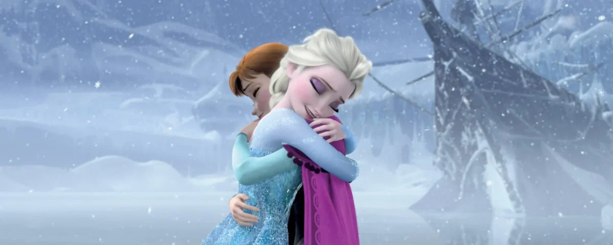 Elsa et Anna de « La Reine des Neiges » s'embrassent dans un paysage enneigé, exprimant un moment d'amour fraternel et de véritable réconciliation.