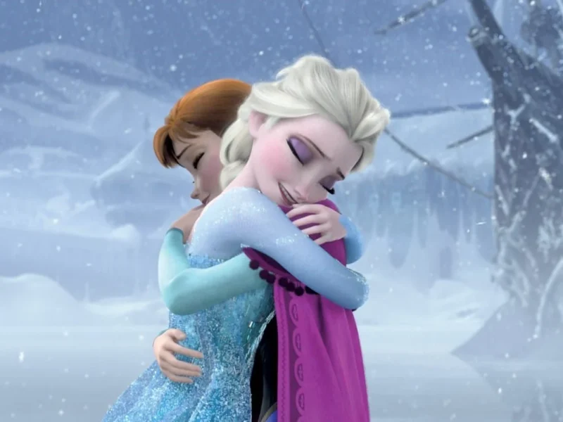 Elsa et Anna de « La Reine des Neiges » s'embrassent dans un paysage enneigé, exprimant un moment d'amour fraternel et de véritable réconciliation.