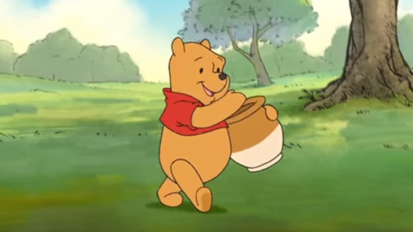 Winnie l'ourson marchant joyeusement avec un pot de miel à la main dans une clairière ensoleillée et herbeuse.