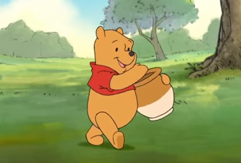 Winnie l'ourson marchant joyeusement avec un pot de miel à la main dans une clairière ensoleillée et herbeuse.