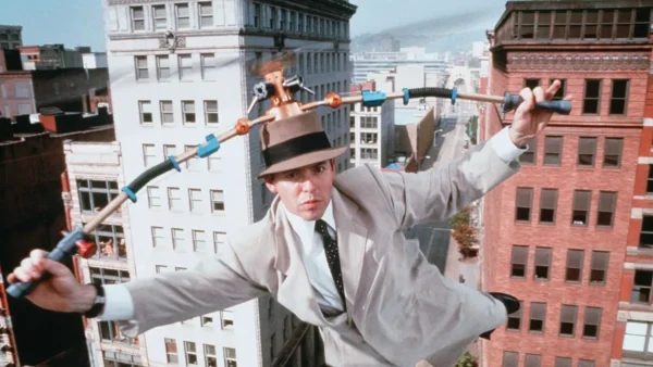 Un homme portant un fedora exécute un numéro d'équilibriste sur un fil électrique entre les bâtiments, utilisant un engin à plusieurs poignées pour maintenir l'équilibre lors de l'événement "Le Noël de Mickey".