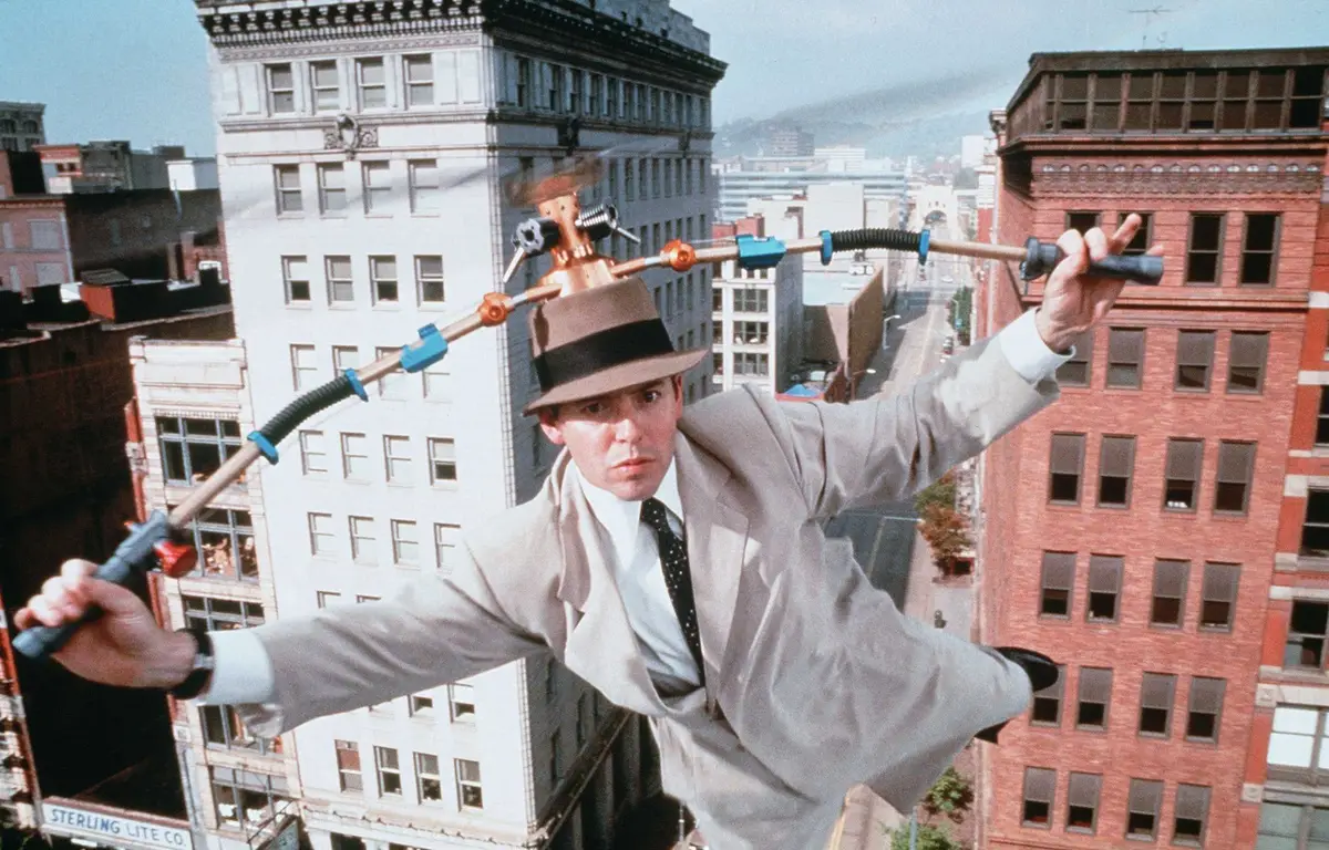 Un homme portant un fedora exécute un numéro d'équilibriste sur un fil électrique entre les bâtiments, utilisant un engin à plusieurs poignées pour maintenir l'équilibre lors de l'événement "Le Noël de Mickey".