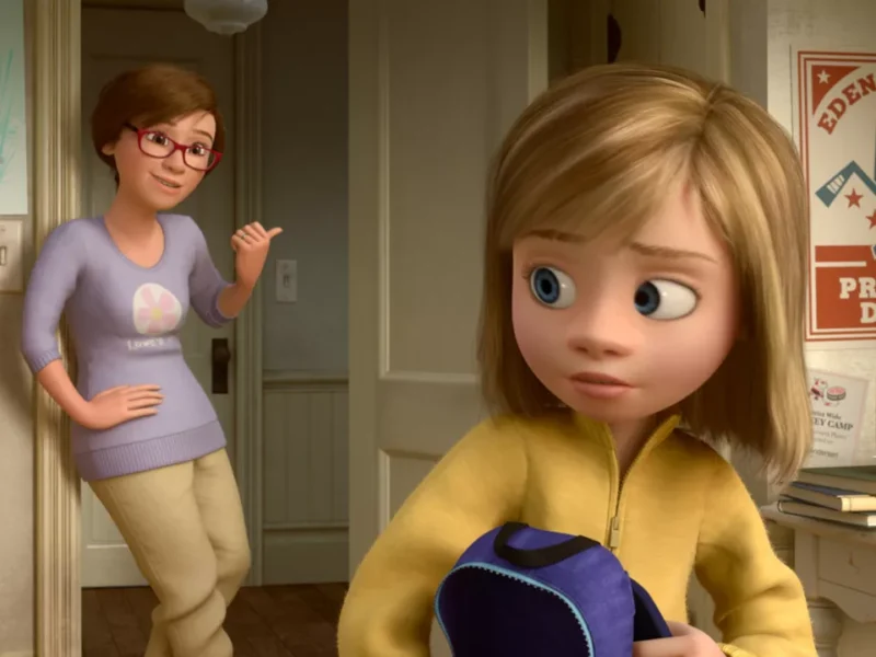 Une image CGI du film d'animation "Inside Out" montrant une jeune fille aux cheveux blonds tenant un sac à dos tandis qu'une femme, vraisemblablement sa mère, se tient dans l'embrasure d'une porte et lui sourit lors de son premier rendez-vous.