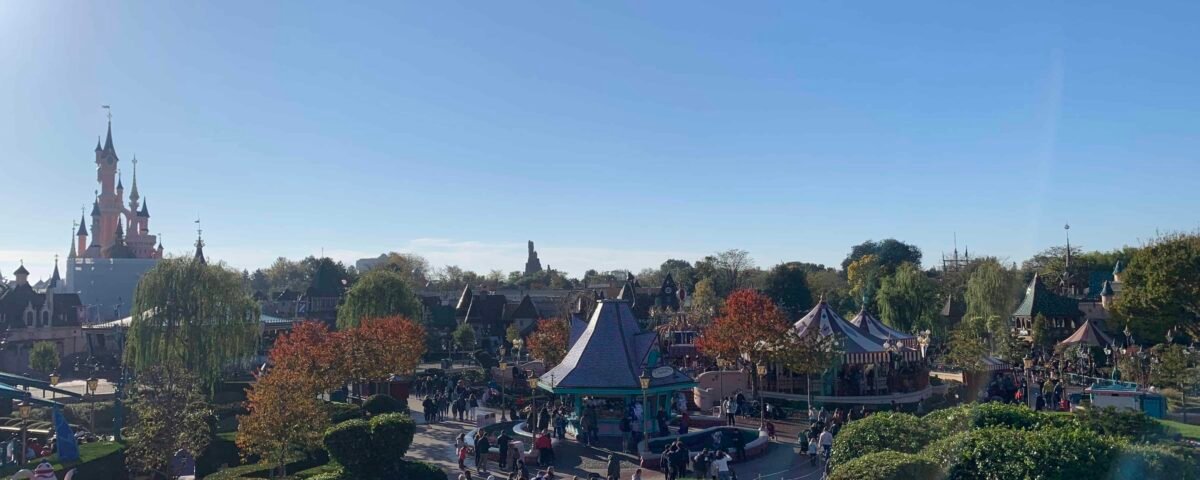 Une vue panoramique de Disneyland Paris mettant en vedette l'emblématique château de la Belle au bois dormant, une verdure luxuriante et des visiteurs animés du parc sous un ciel ensoleillé.