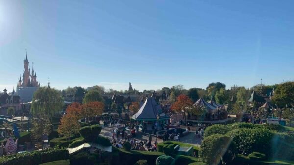 Une vue panoramique de Disneyland Paris mettant en vedette l'emblématique château de la Belle au bois dormant, une verdure luxuriante et des visiteurs animés du parc sous un ciel ensoleillé.