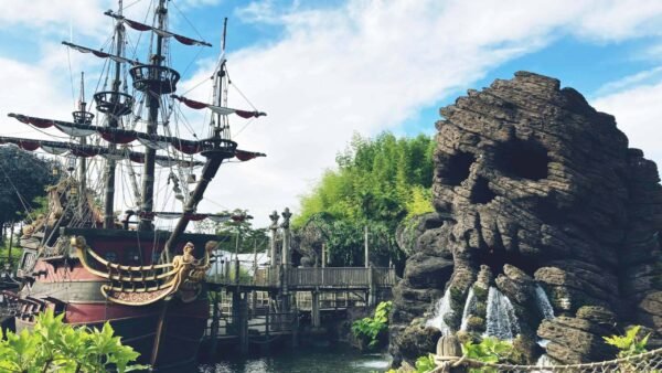 Une zone imaginative sur le thème des pirates à Disneyland avec un grand bateau pirate détaillé ancré à côté d'une formation rocheuse accidentée en forme de crâne avec des cascades. Une passerelle en bois et de la verdure rehaussent la vue panoramique.