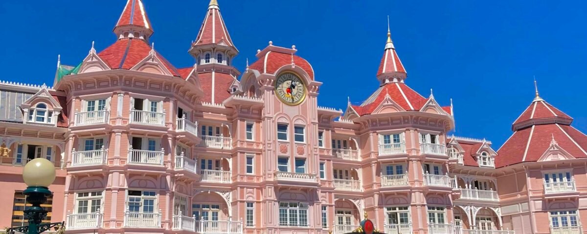 Une image vibrante de l'Hôtel Disney, mettant en valeur la façade rose et les toits ornés d'un bâtiment inspiré des contes de fées sous un ciel bleu clair.