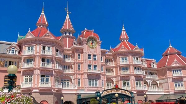 Une image vibrante de l'Hôtel Disney, mettant en valeur la façade rose et les toits ornés d'un bâtiment inspiré des contes de fées sous un ciel bleu clair.