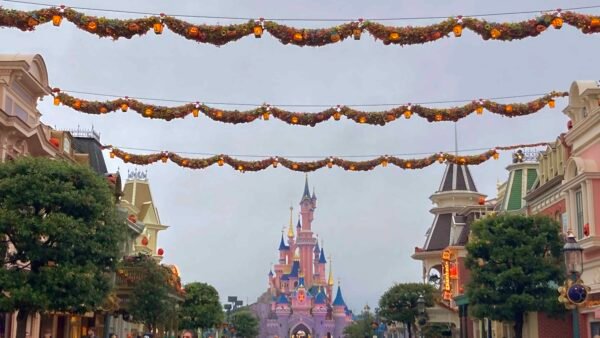 Des décorations d'automne sont suspendues au-dessus d'une rue bordée de bâtiments colorés menant à Disneyland Paris par temps couvert.