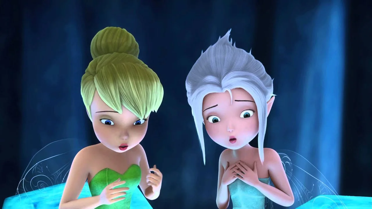 Deux personnages de fées animés aux visages expressifs, l'un aux cheveux blonds et à la robe verte ressemblant aux yeux doux de Dumbo, l'autre aux cheveux blancs et au haut bleu, apparaissent surpris et inquiets dans un décor faiblement éclairé.