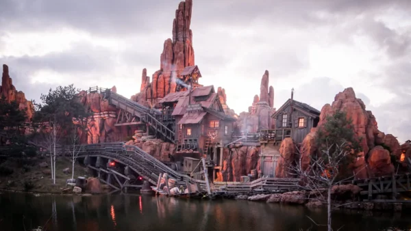 Une vue panoramique d'un paysage montagneux et accidenté avec un village en bois et des ponts au crépuscule, se reflétant dans un lac tranquille en contrebas, rappelant Disneyland Paris.