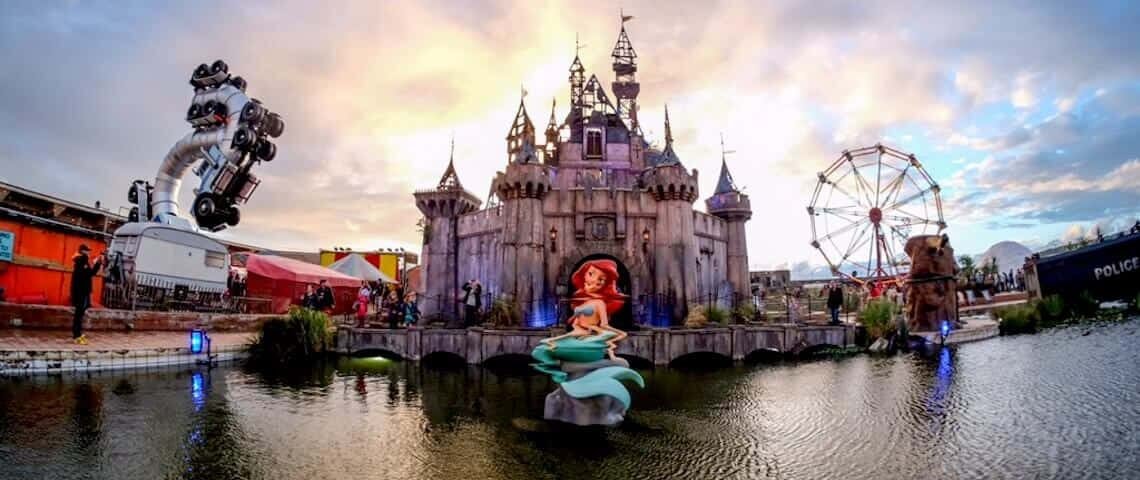 Une scène fantastique du parc à thème Disneyland mettant en vedette un grand château, une grande roue et un robot, avec une statue d'Ariel de La Petite Sirène au premier plan un étang réfléchissant sous un ciel dramatique