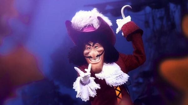 Une personne habillée en capitaine crochet avec un grand chapeau, un manteau rouge et un crochet en guise de main, posant de manière ludique sur un arrière-plan sombre et flou.