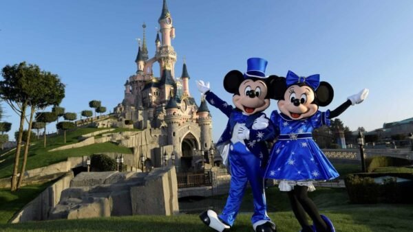 Mickey et Minnie Mouse en tenues bleues posant joyeusement devant le château de la Belle au bois dormant à Disneyland Paris par une journée ensoleillée.
