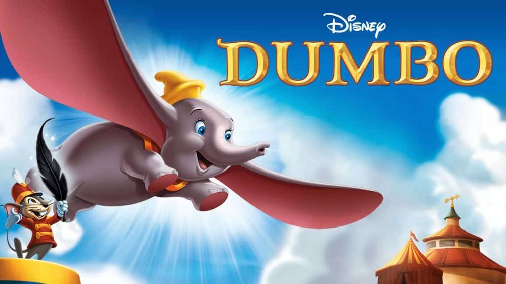 Graphique promotionnel pour « Dumbo » de Disney représentant un Dumbo souriant volant avec de grandes oreilles étendues et Timothy Q. Mouse applaudissant, sur un ciel bleu vif et des chapiteaux de cirque en arrière-plan.