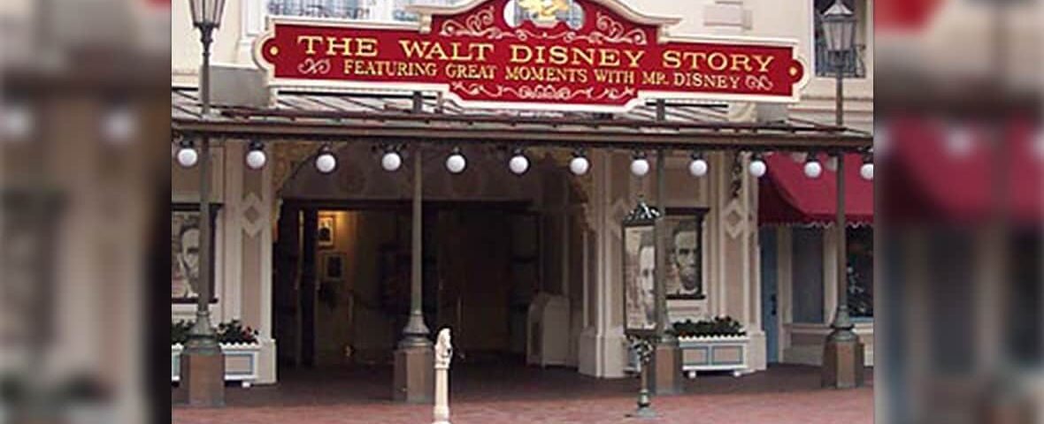 L'entrée de l'attraction « The Walt Disney Story » affiche un panneau rouge orné de bordures dorées, flanqué de grandes affiches de portraits, dans un parc à thème Disney.