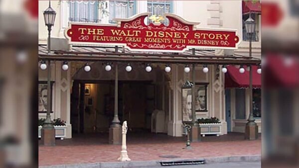 L'entrée de l'attraction « The Walt Disney Story » affiche un panneau rouge orné de bordures dorées, flanqué de grandes affiches de portraits, dans un parc à thème Disney.