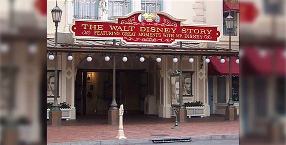L'entrée de l'attraction « The Walt Disney Story » affiche un panneau rouge orné de bordures dorées, flanqué de grandes affiches de portraits, dans un parc à thème Disney.