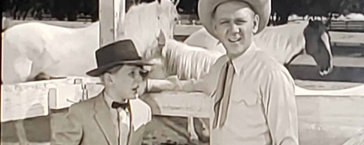 Une image en noir et blanc tirée de « Les Aventures de Spin et Marty » représentant deux hommes dans un ranch ; l'un portant un costume et un nœud papillon, et l'autre en tenue décontractée avec un chapeau de cowboy,
