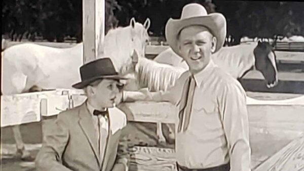 Une image en noir et blanc tirée de « Les Aventures de Spin et Marty » représentant deux hommes dans un ranch ; l'un portant un costume et un nœud papillon, et l'autre en tenue décontractée avec un chapeau de cowboy,