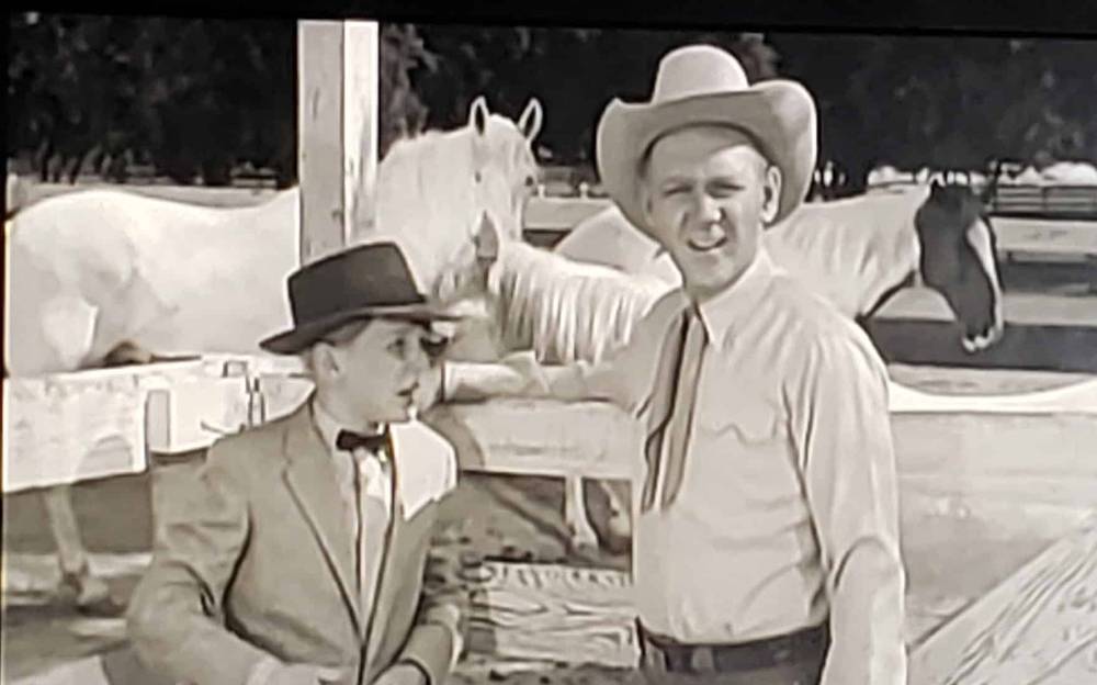 Une image en noir et blanc tirée de « Les Aventures de Spin et Marty » représentant deux hommes dans un ranch ; l'un portant un costume et un nœud papillon, et l'autre en tenue décontractée avec un chapeau de cowboy,