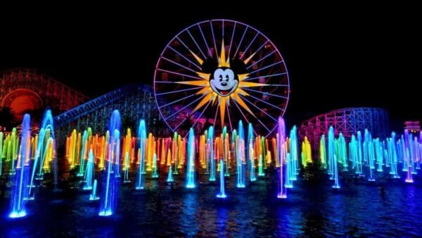 Scène nocturne colorée mettant en vedette une grande roue avec une silhouette de Mickey Mouse illuminée, entourée de luminaires vibrants et multicolores et d'autres structures éclairées.