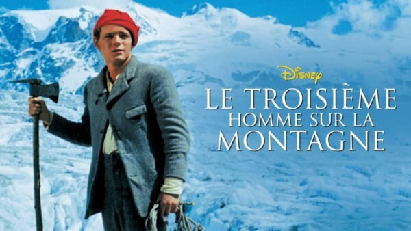 Un homme au bonnet rouge et en tenue d'alpinisme traditionnelle tenant une pioche se tient devant un fond de montagne enneigée, avec le texte « le troisième homme sur la montagne » superposé.