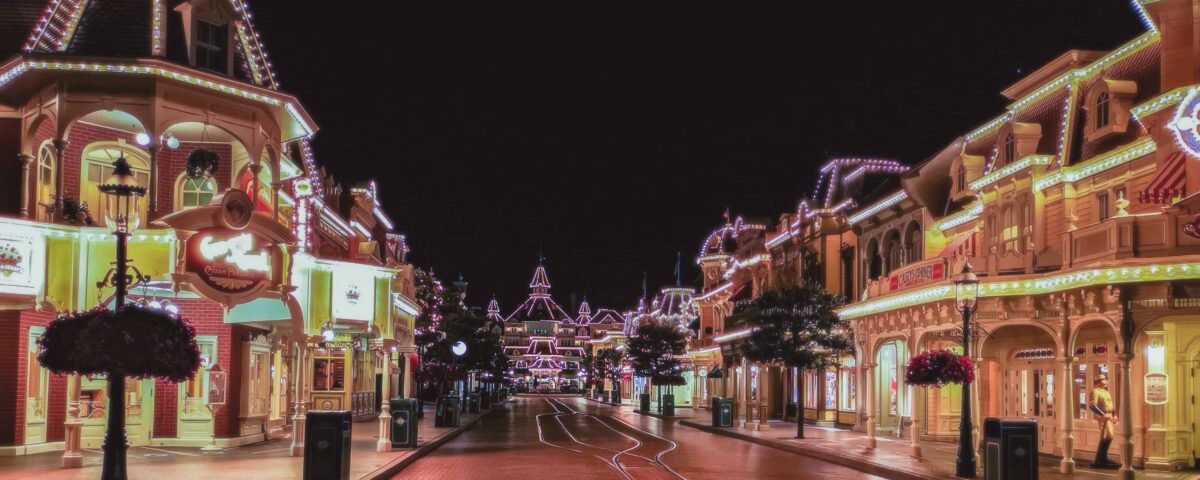Vue nocturne d'une rue principale vide de Disneyland Paris, magnifiquement éclairée par des lumières colorées, mettant en valeur des bâtiments de style victorien et des décorations festives.