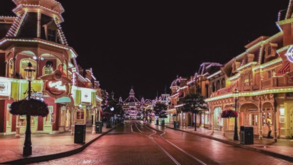 Vue nocturne d'une rue principale vide de Disneyland Paris, magnifiquement éclairée par des lumières colorées, mettant en valeur des bâtiments de style victorien et des décorations festives.
