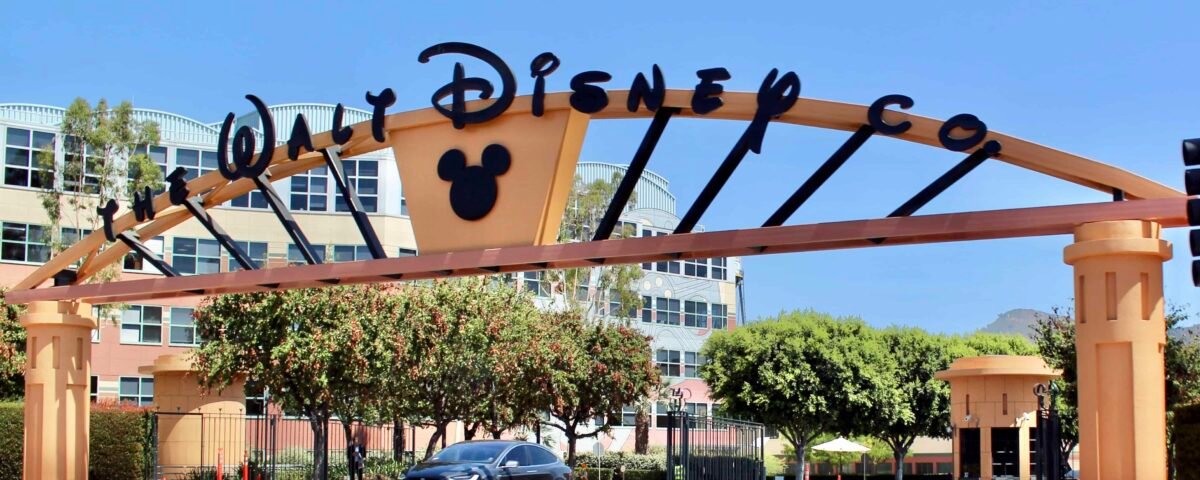 Panneau d'arche indiquant « Disney » avec la silhouette de Mickey Mouse, encadrant une voiture qui passe par une journée ensoleillée avec un ciel bleu clair.