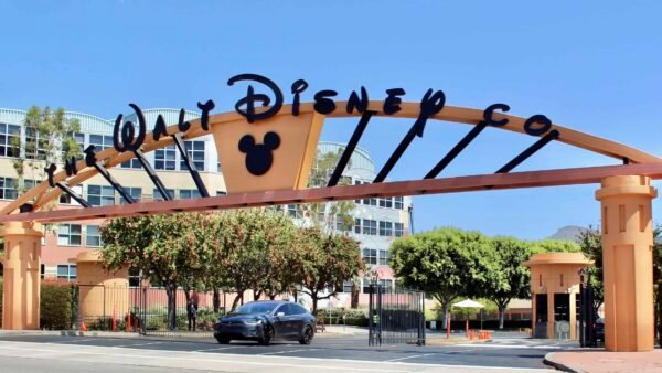 Panneau d'arche indiquant « Disney » avec la silhouette de Mickey Mouse, encadrant une voiture qui passe par une journée ensoleillée avec un ciel bleu clair.