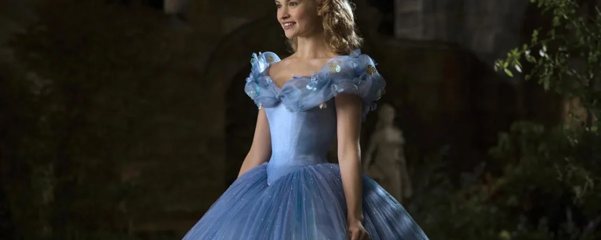 Une femme habillée en Cendrillon se tient dans une grande cour. Elle porte une élégante robe bleue avec de délicats accents floraux et ses cheveux sont coiffés d'un chignon orné. Le décor est la nuit,