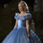 Une femme habillée en Cendrillon se tient dans une grande cour. Elle porte une élégante robe bleue avec de délicats accents floraux et ses cheveux sont coiffés d'un chignon orné. Le décor est la nuit,