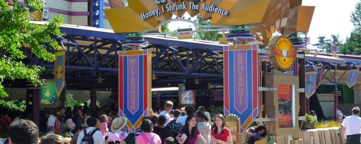 Les visiteurs se rassemblent à l'entrée de l'attraction Disneyland « Chérie, j'ai rétréci le public » sous une grande pancarte accueillant le public, aux éléments de design vibrants et colorés.