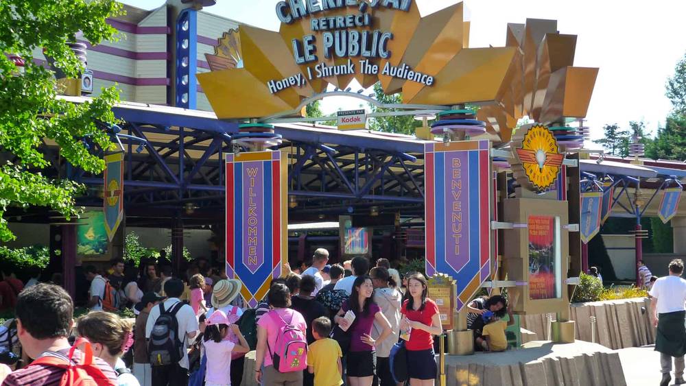 Les visiteurs se rassemblent à l'entrée de l'attraction Disneyland « Chérie, j'ai rétréci le public » sous une grande pancarte accueillant le public, aux éléments de design vibrants et colorés.