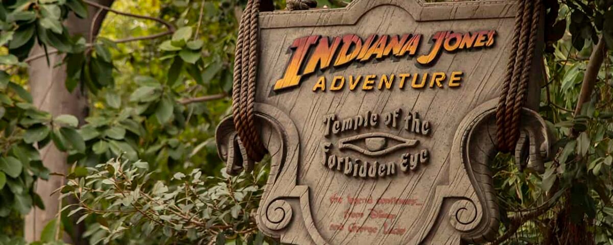 Un panneau en bois patiné pour l'attraction « Indiana Jones Adventure : Temple of the Forbidden Eye », suspendu à d'épaisses cordes sur fond de feuillage vert dense.