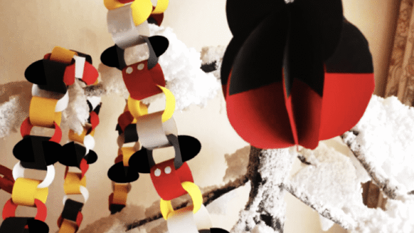 Une scène artisanale comprenant des chaînes en papier rouge, jaune et noir, ainsi qu'un grand ornement en papier en forme de tête de Mickey, sur un fond blanc comme neige.