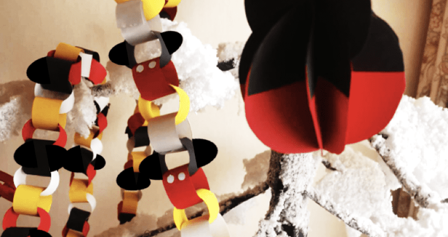 Une scène artisanale comprenant des chaînes en papier rouge, jaune et noir, ainsi qu'un grand ornement en papier en forme de tête de Mickey, sur un fond blanc comme neige.