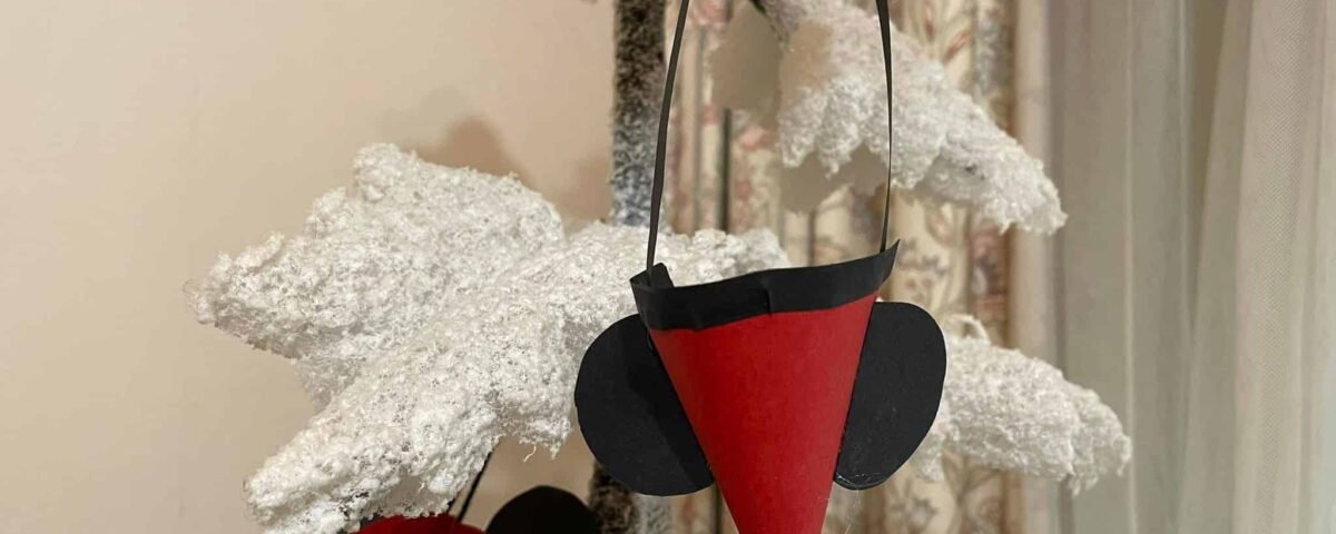 Un sapin de Noël artificiel saupoudré de neige orné de décorations uniques, dont une paire d'écouteurs Mickey noir et rouge et un cercle rouge et noir avec un carré jaune.