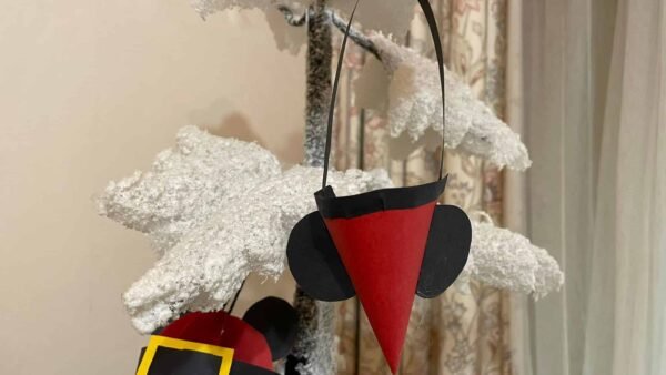 Un sapin de Noël artificiel saupoudré de neige orné de décorations uniques, dont une paire d'écouteurs Mickey noir et rouge et un cercle rouge et noir avec un carré jaune.