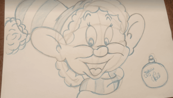 Croquis au crayon d'un elfe joyeux de bande dessinée avec un grand sourire, portant un simple chapeau. À côté de l'elfe, une décoration de Noël inscrite « Joyeuses fêtes » est dessinée.