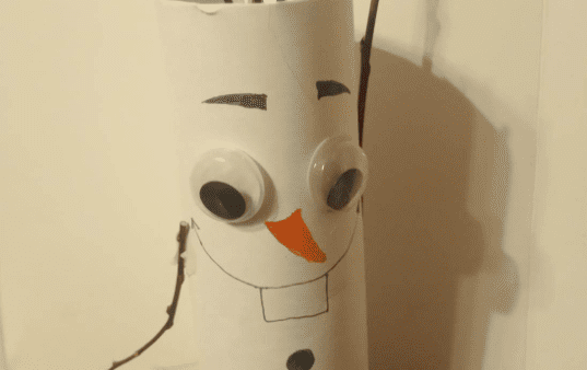 Un Olaf fait main fabriqué à partir d'un rouleau de papier toilette, avec des bras en brindilles, des yeux écarquillés, un nez de carotte en papier et des traits du visage et des boutons dessinés.