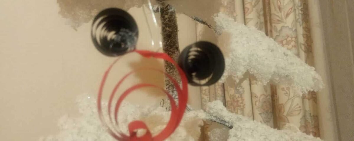 Gros plan d'un ornement Mickey fantaisiste fabriqué à la main avec un cadre rouge circulaire avec des détails en spirale et deux perles noires suspendues près du sommet, sur un tissu décoratif doux et blanc en arrière-plan.