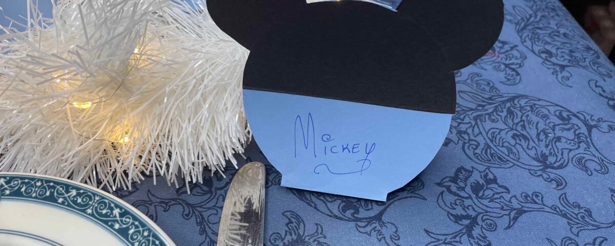 Un espace réservé en papier en forme de Mickey Mouse avec l'inscription « Mickey » dessus, dans une salle à manger avec un sapin de Noël blanc et une nappe bleue.