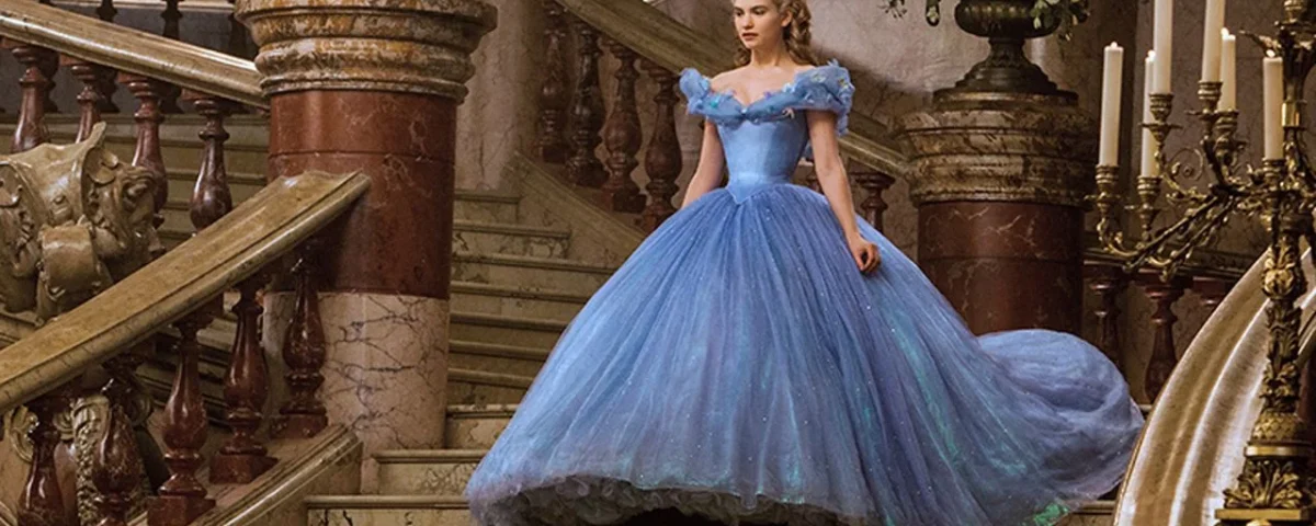 Une femme vêtue d'une élégante robe de bal bleue se tient sur un grand escalier dans une pièce luxueuse et ornée de bougies et d'un grand bouquet de fleurs, incarnant la grâce de Cendrillon.