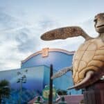 Une statue de Crush, la tortue du Monde de Nemo, devant les studios Walt Disney, avec des peintures murales aux couleurs vives représentant des scènes sous-marines, sous un ciel clair du soir.