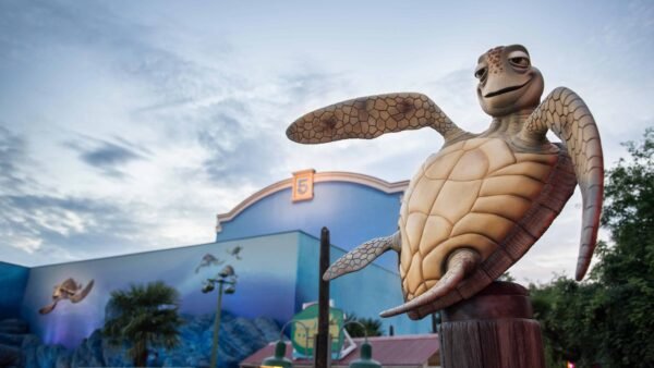 Une statue de Crush, la tortue du Monde de Nemo, devant les studios Walt Disney, avec des peintures murales aux couleurs vives représentant des scènes sous-marines, sous un ciel clair du soir.